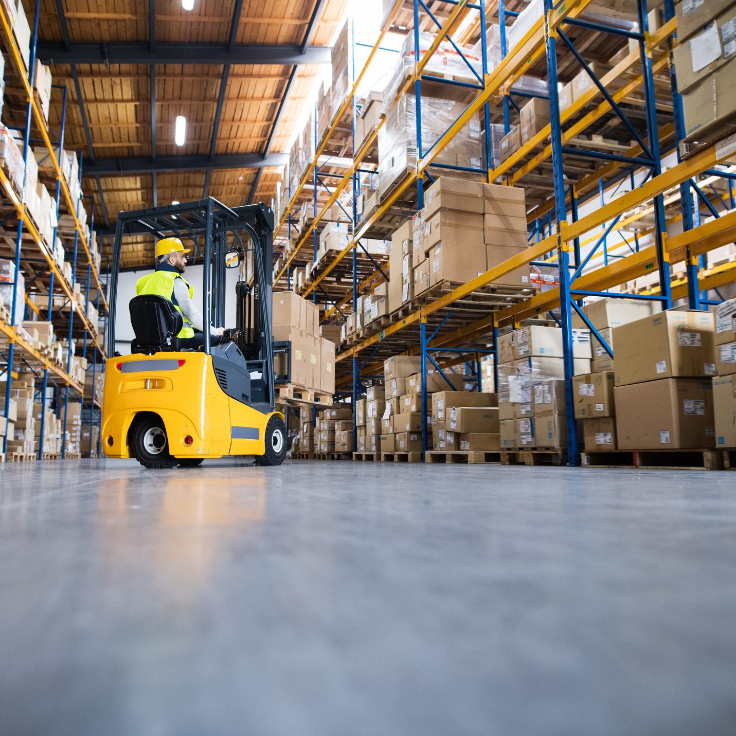 Young male worker lowering a pallet with boxes. Forklift driver working in a warehouse.